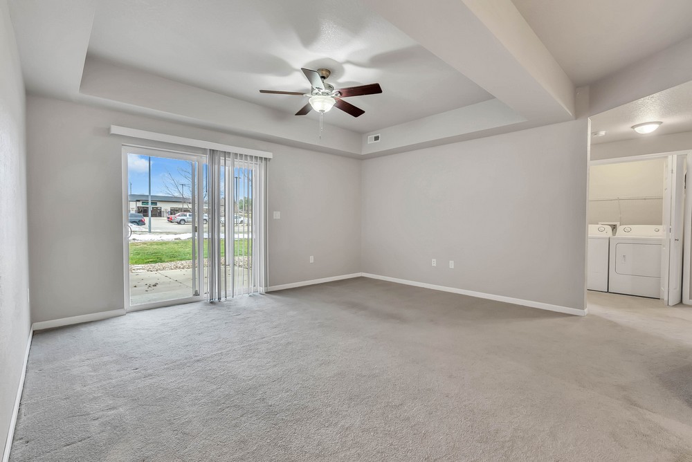 View across living room with sliding patio doors open with vertical blinds and ceiling light and fan.
