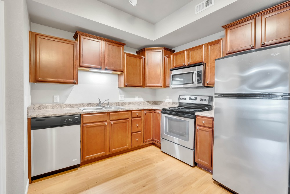 Kitchen with brown cabinets, neutral countertop, double sink, dish washer, fridge, and microwave above stove and oven.